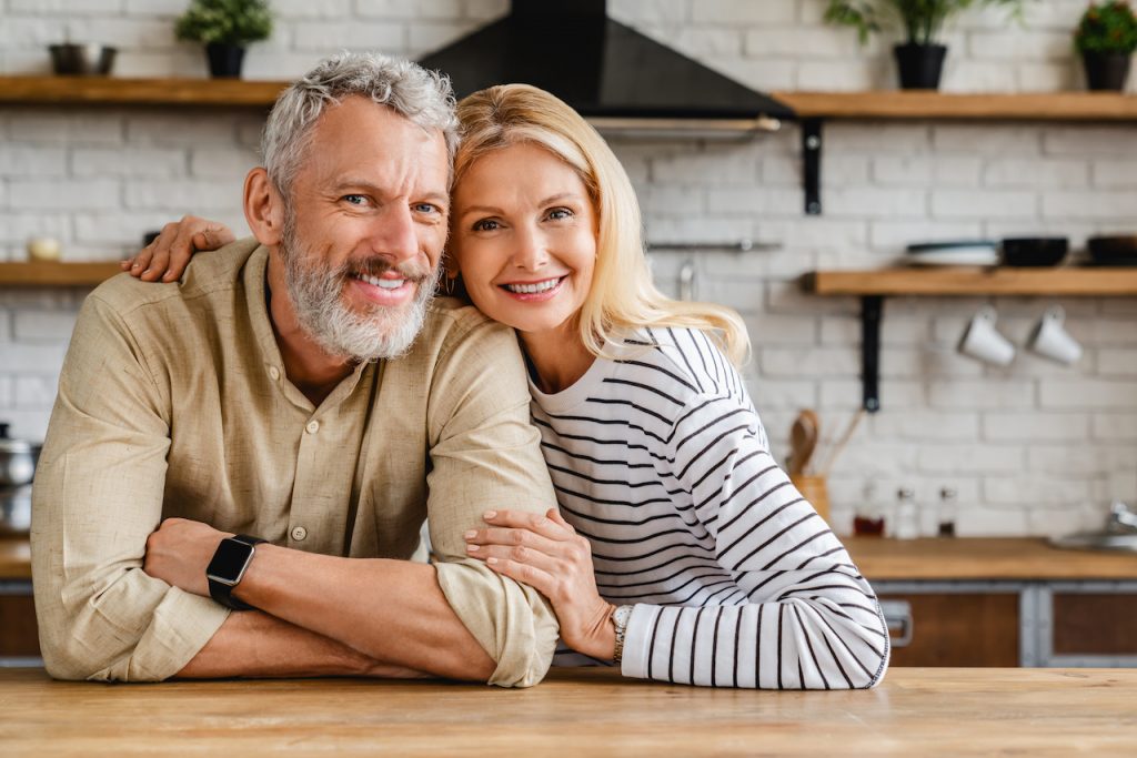 Portrait of middle aged couple hugging while standing together in kitchen at home